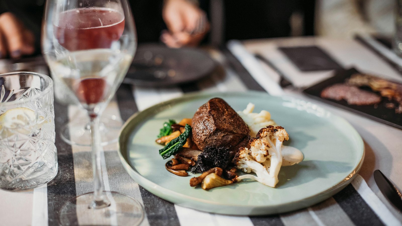Elegant plated Colorado beef tenderloin and Palisade peach galette on fine dinnerware with wine glasses.