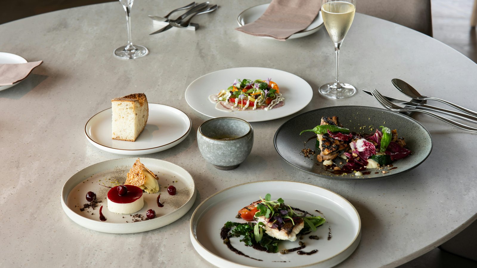 Elegant plated dish on a modern dining table with Denver skyline visible through floor-to-ceiling windows.