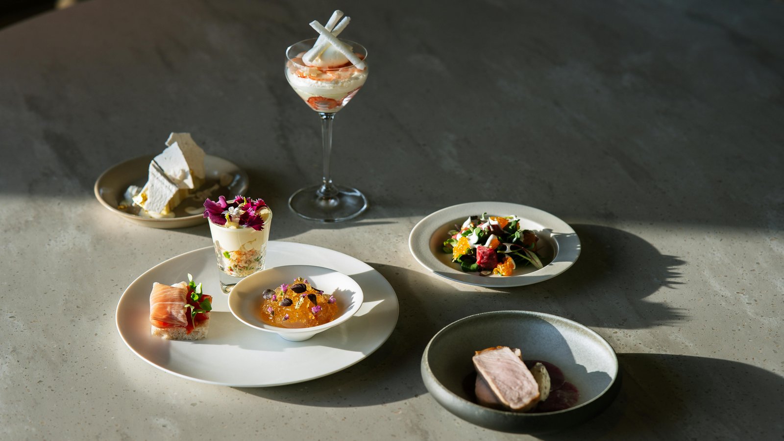 Chef presenting an elegant plated course with snow-capped Teton peaks visible through a chalet window.