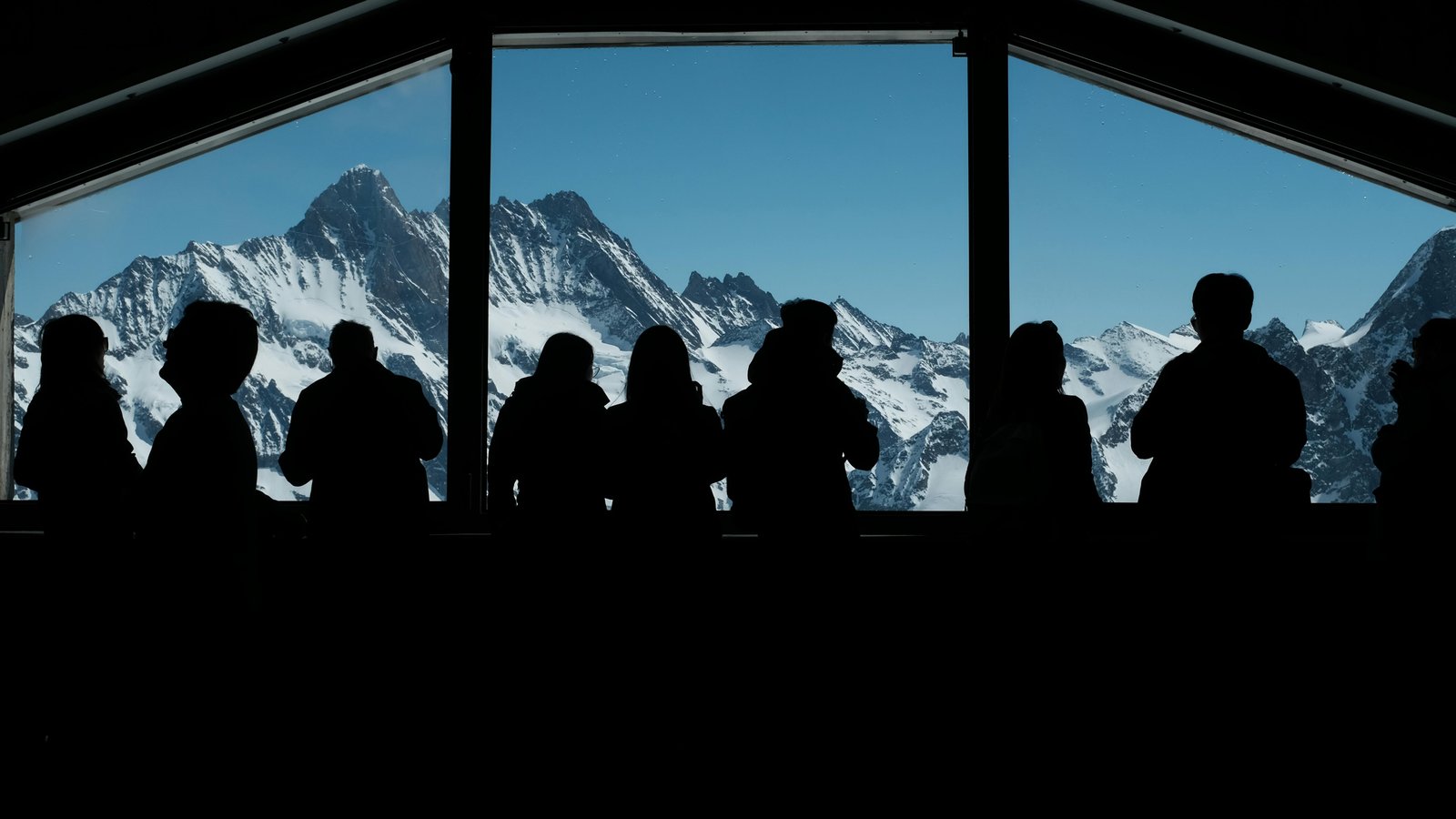 Gourmet plated dinner with mountain views through floor-to-ceiling windows overlooking snow-covered peaks.